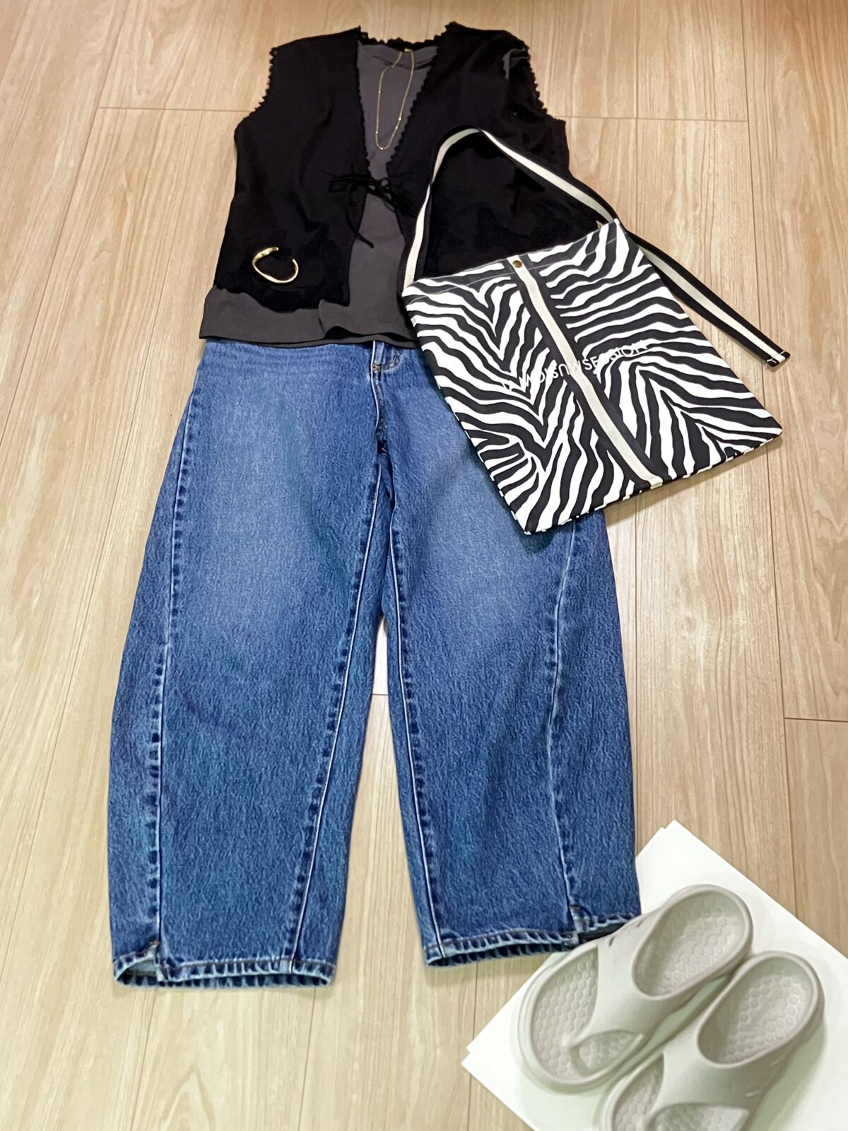 黒のベストとタンクトップ、デニムのワイドパンツ、ゼブラ柄のバッグ、白いサンダルを並べたコーデ