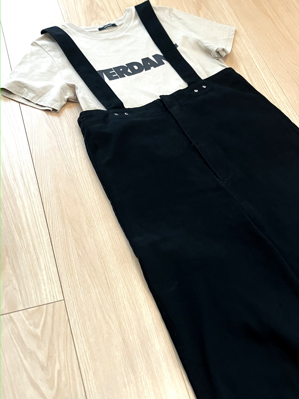 黒のサロペットに、ベージュのプリントTシャツを合わせたコーデ