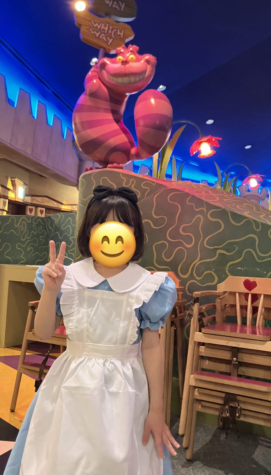 アリスの衣装を着た娘。チェシャ猫の装飾の前で(顔はスタンプで隠しています)